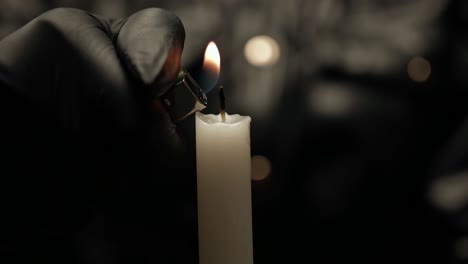 A-person-wearing-black-gloves-lighting-a-candle-with-a-lighter,-close-up-of-a-candle-with-bokeh