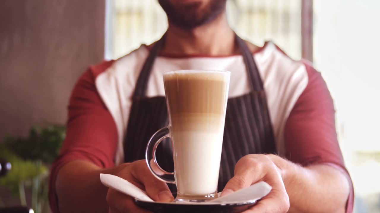 camarero sonriente sosteniendo un vaso de café frío en una cafetería