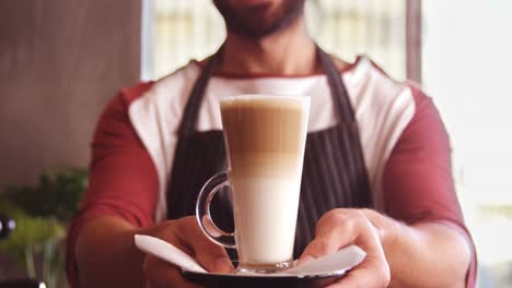 Smiling-waiter-holding-glass-of-cold-coffee-in-cafe