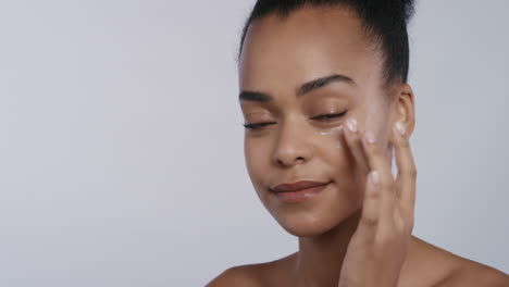 portrait beautiful young african american woman applying skin cream moisturizer on face enjoying exfoliation massaging luxury anti aging lotion perfect feminine beauty on white background skincare concept