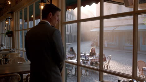 man in a suit looking out from a cafe window at an outdoor street scene