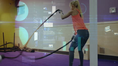 fitness data tracking animation over woman exercising with battle ropes in gym