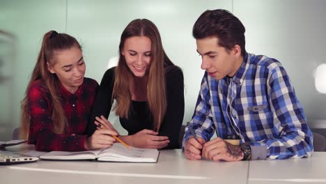 Estudiantes-Sonrientes-Trabajando-En-Su-Tarea-Sentados-Juntos-En-La-Mesa-Y-Tomando-Café.-Grupo-De-Jóvenes-En-La-Reunión-En-Un-Apartamento-Moderno.-Toma-En-Cámara-Lenta