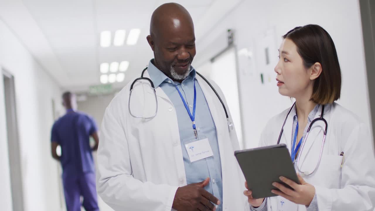 Video of diverse male and female doctor with tablet talking in hospital corridor, copy space