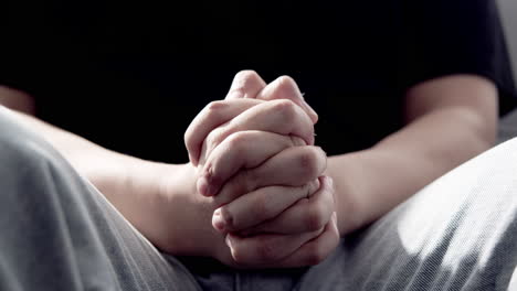 man sitting with his hands clasped, symbolizing the burdens he faces from relentless work and emotional distress.