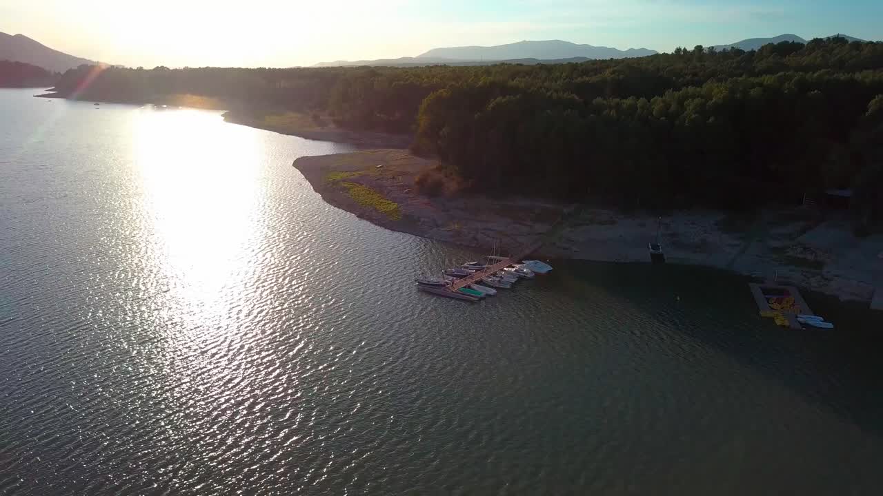 Aerial ascending shot of a woman sitting in a pier with boats moored during the sunset