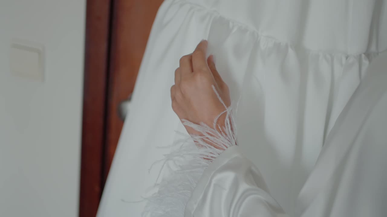 Bride's hand gently touching a white wedding dress with feathered sleeves