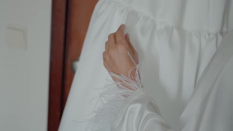bride's hand gently touching a white wedding dress with feathered sleeves
