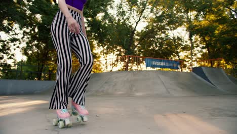 primer plano: una chica joven con un corte de pelo corto en una camiseta púrpura y pantalones a rayas patines en un parque de patinaje en una superficie de hormigón. actividades al aire libre en verano