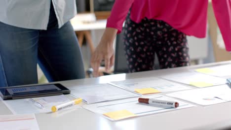 diverse colleagues discussing work with documents on table and tablet in office in slow motion