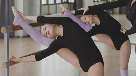 dos chicas rubias gimnásticas ensayando un movimiento de ballet frente a la barra de ballet 4