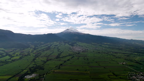 Backwards-drone-shot-showing-the-snowy-top-of-the-popocatepetl-volcano-in-mexico-city-and-the-city-of-amecameca