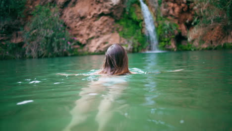 swimsuit model swimming fjord back view. woman floating in deep emerald lagoon