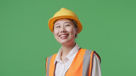 close up side view of asian female engineer with safety helmet looking around while standing in the green screen background studio