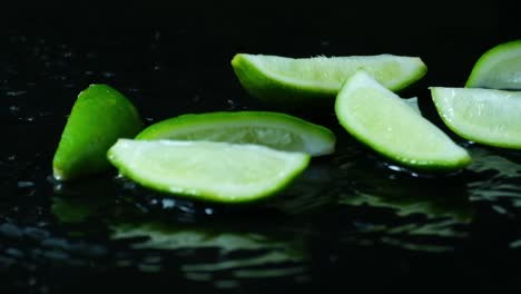 a bunch of sliced limes fall into frame splashing water on a black background