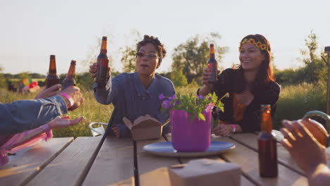 group of young friends at music festival sitting around table and drinking beer