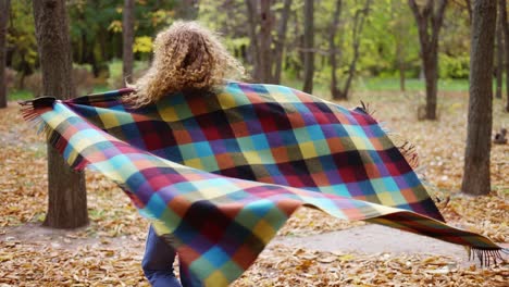 curly girl in golden autumn park covering herself in plaid spinning around and smiling