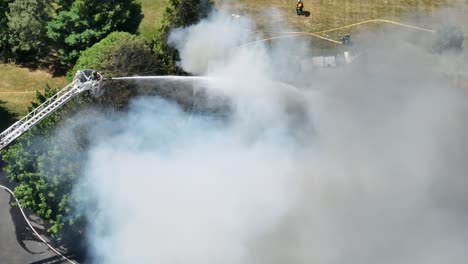 bombero en la escalera con la manguera de agua rociando en la casa en llamas en un día soleado