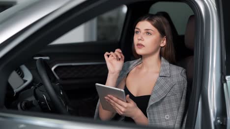 chica adulta con estilo en un traje de negocios con una tableta sentada en el coche