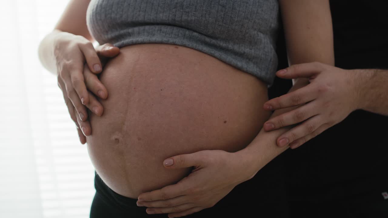 Dettaglio di madre in gravidanza avanzata e futuro padre che toccano l'addome.