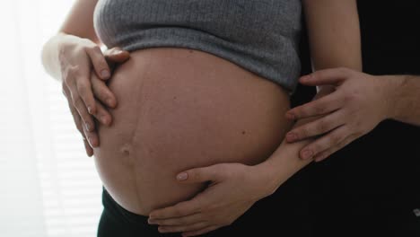 detail of mother in advanced pregnancy and future father touching the abdomen.