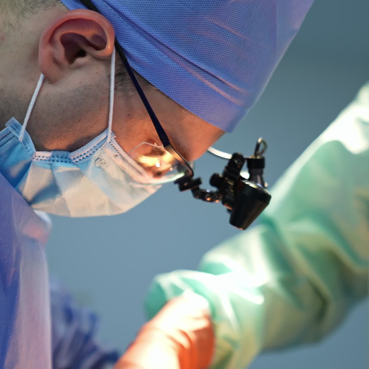 Hardworking male surgeon with device glasses bent low over the patient. Portrait close up of a medical specialist. Side view