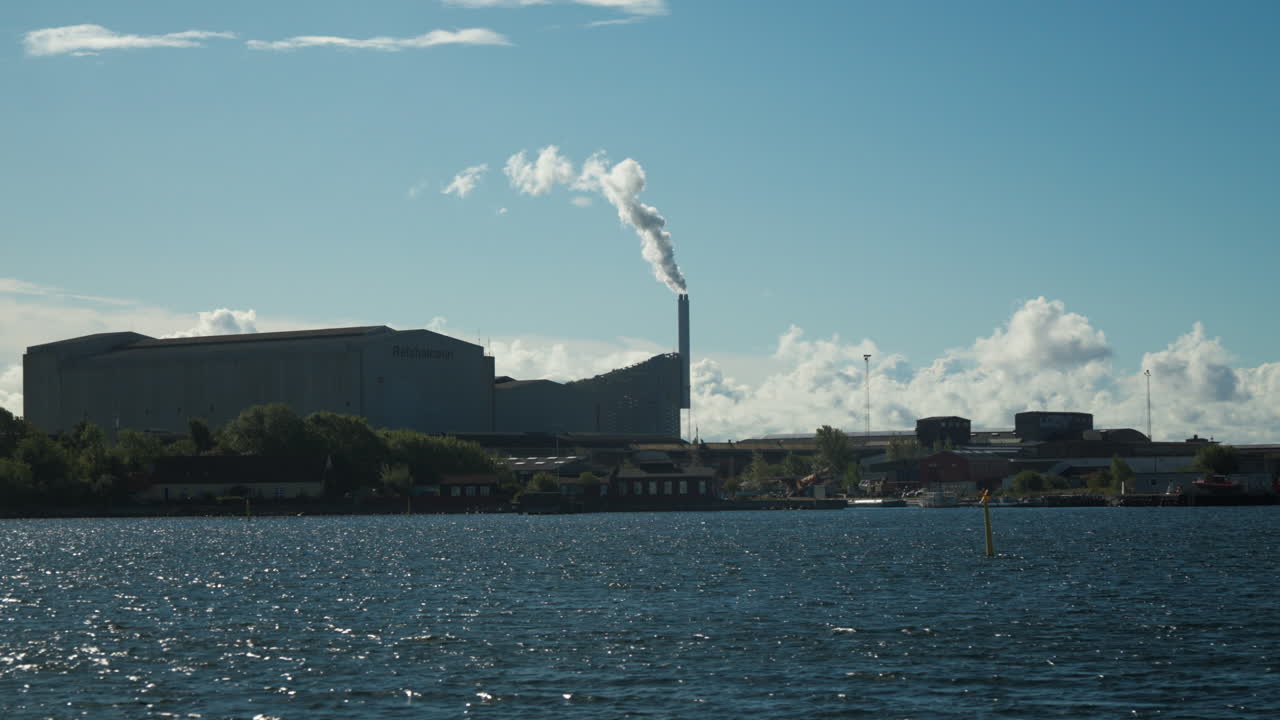 Industrial skyline with smoke stack by water. Perfect for environmental documentaries or cityscape projects.