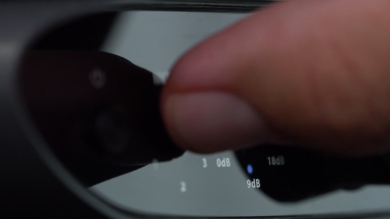 Macro shot of finger pressing input button on black audio interface panel with gain knob visible