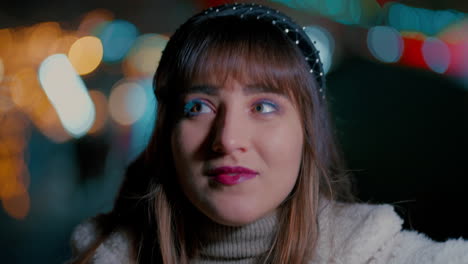 cerca de la cara de una joven hermosa mujer mirando hacia arriba y alrededor con las coloridas luces de navidad bokeh del mercado de navidad en el fondo durante una fría noche de invierno en cámara lenta