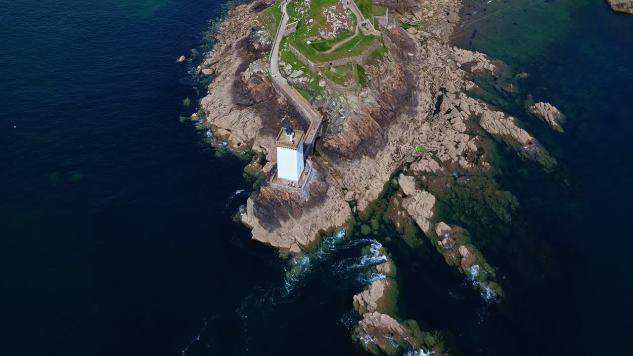 Top-down drone shot panning smoothly over the Kermorvan lighthouse and rocky coastline in Le Conquet, Brittany. - France
