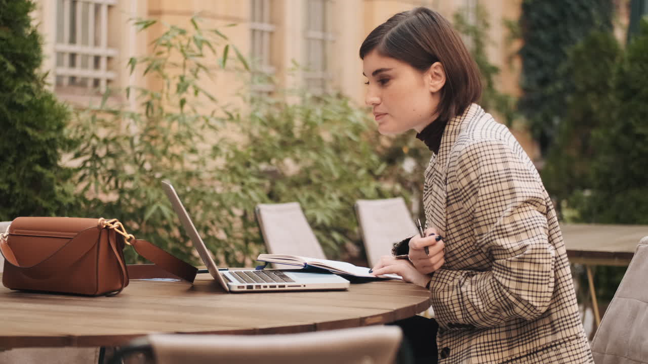 Businesswoman working on laptop in cafe outdoor.