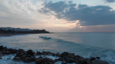 forward-drone-shot-over-rocks-in-seacoast-as-waves-wash-break-during-cloudy-golden-hour