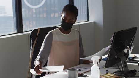 African-american-businesswoman-wearing-face-mask,-working-in-office