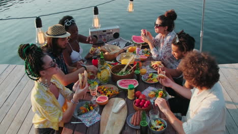 company of diverse friends having dinner party on lake pier