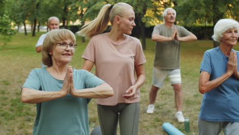 female yoga instructor helping senior people during outdoor practice