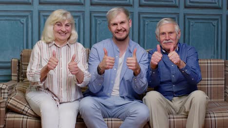 family of senior grandparents with adult son showing thumbs up gesture having fun looking at camera