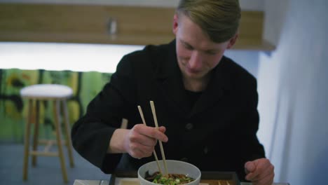 close up view of a man trying to eat noodles using chopsticks. learning how to hold chopsticks without success and taking a fork