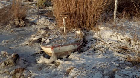 old abandoned frozen wooden boat under white snow at lakeside