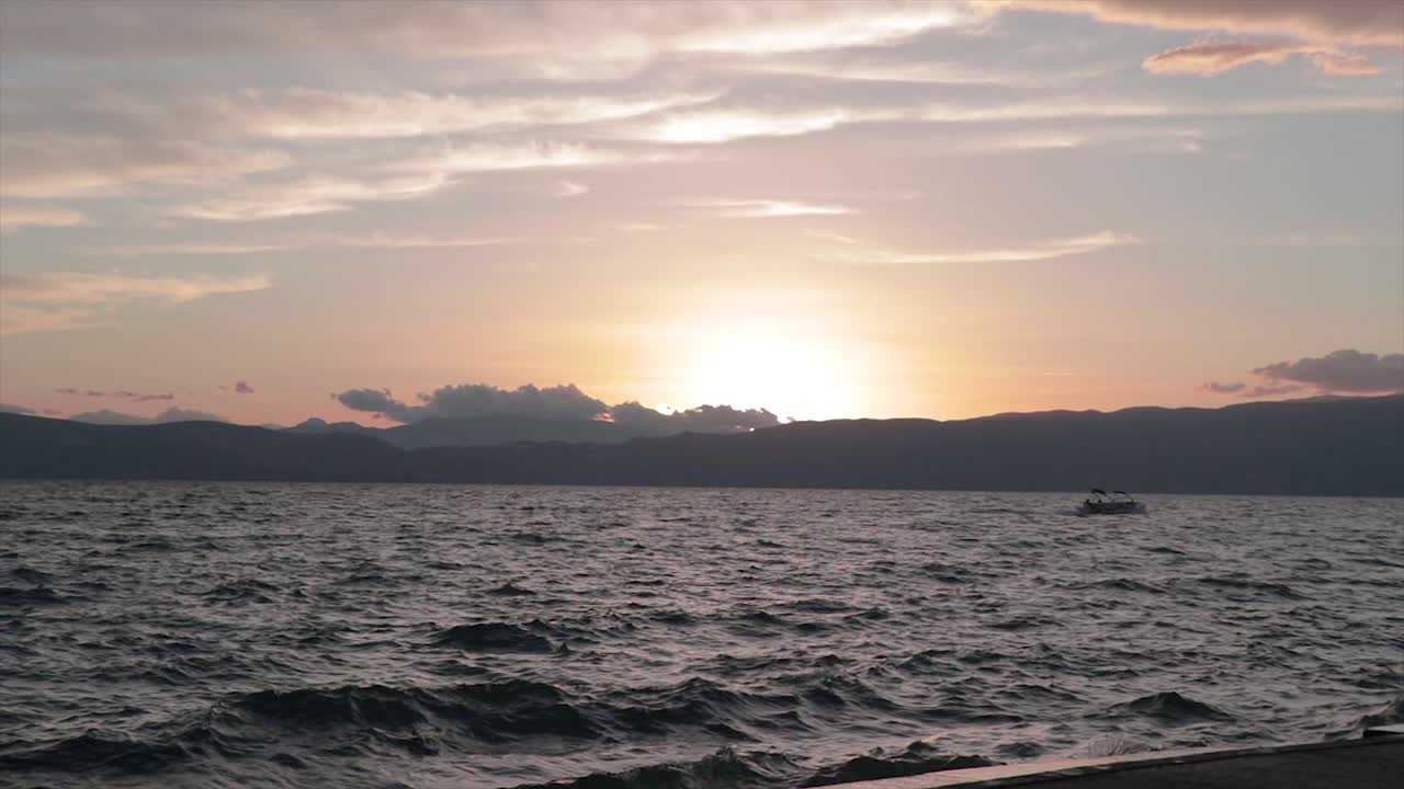 석양에 바람이 부는 폭풍우가 치는 호수에서 물 위를 여행하는 작은 배