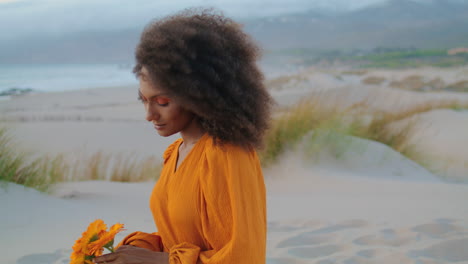 attractive girl admiring flowers sitting on sandy seashore evening close up.