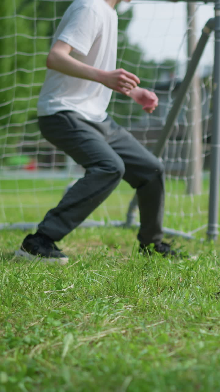 은 셔츠를 입은 어린 소년이 골키퍼가 뛰어내리고 미스하면서 골을 넣은 팀 동료에게 공을 던지는 클로즈업