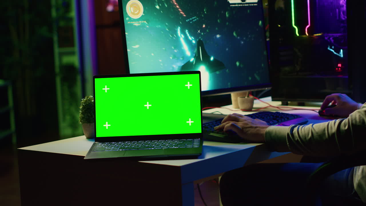 laptop con schermo verde accanto a un uomo che si diverte usando la tastiera di gioco per volare una nave spaziale in un videogioco sf