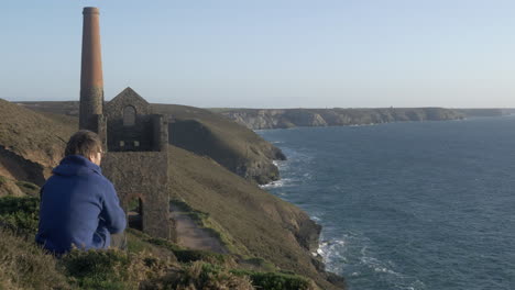 Person-sitting-and-relaxing-with-a-beautiful-coastal-view-of-Cornish-mine,-Copy-Space