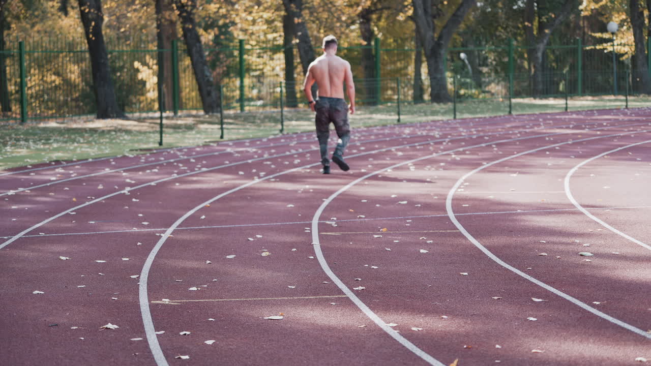 Back view of a man jogging on the stadium. Young athlete practices running outside on athletics track in autumn.