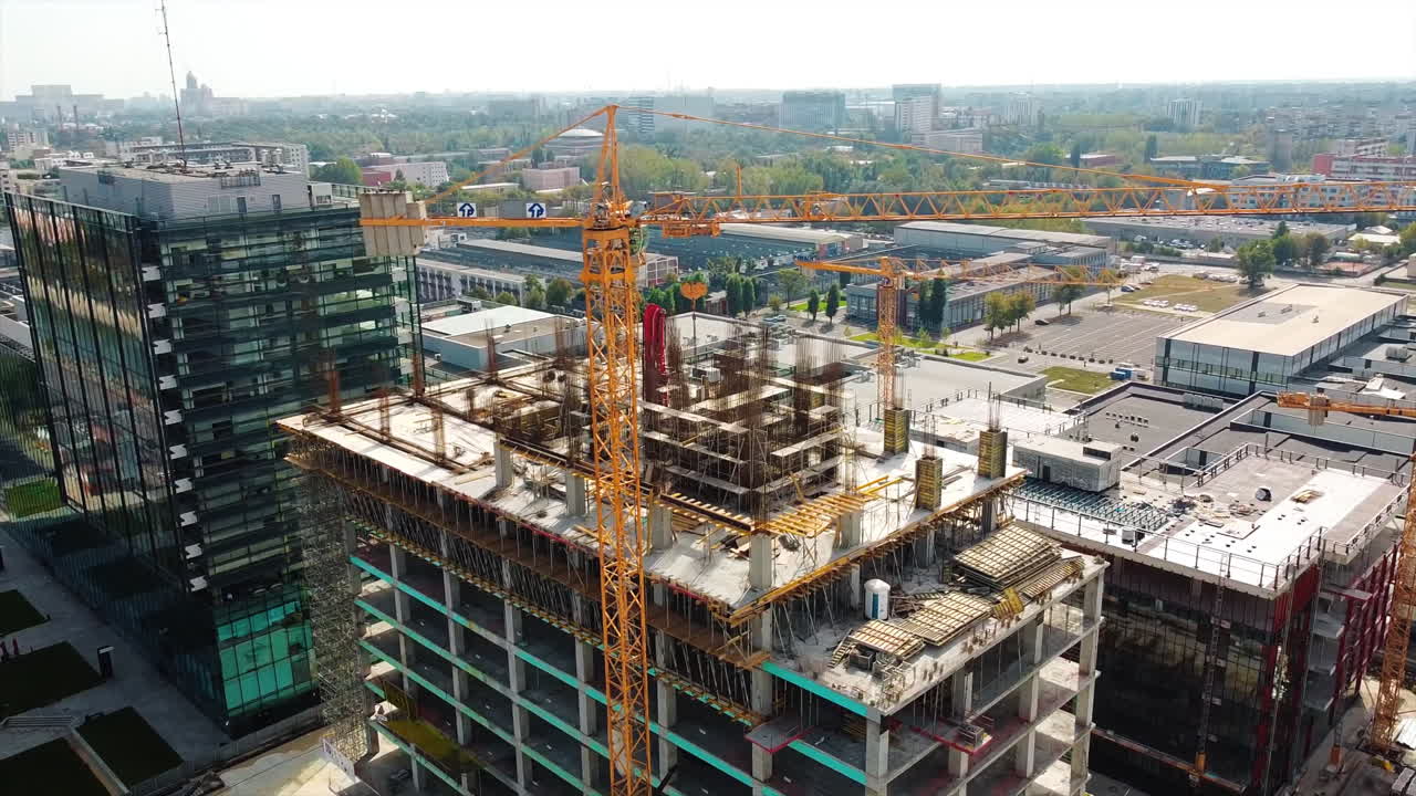 Construction works of a building in business center with scaffolding on the facade and uilding crane, city view and residential buildings. View from the drone