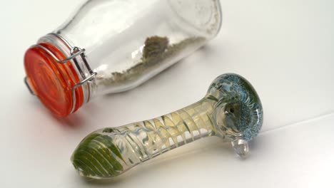 a colorful glass pipe sits next to a clear sealed bottle containing marijuana grounds