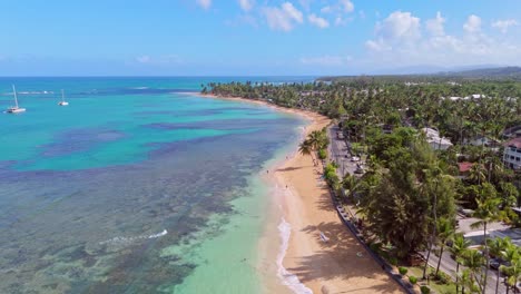 playa punta popy sandy beach during sunny day with coral reef water. aerial top down flyover coastline. driving cars on coastal street with tropical palm trees. wide shot.