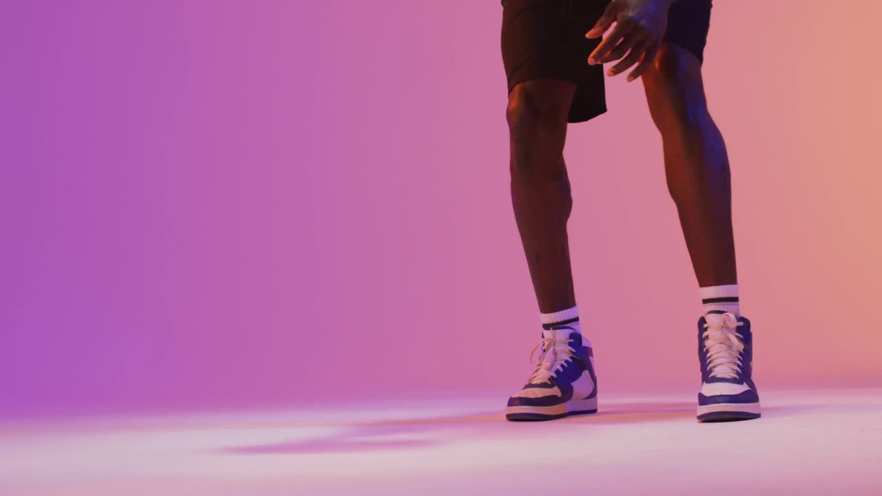 video de una sección baja de un jugador de baloncesto masculino biracial con una pelota en un fondo naranja a rosa.