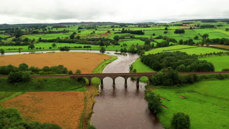 aerial dolly shot looking over a curving river with a railway viaduct crossing the river, bright but cloudy day