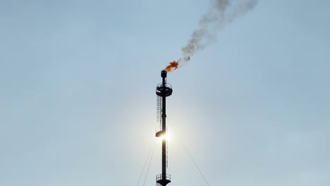 flare stack refinery burning, giant flame and smokestack, sun behind, clear sky